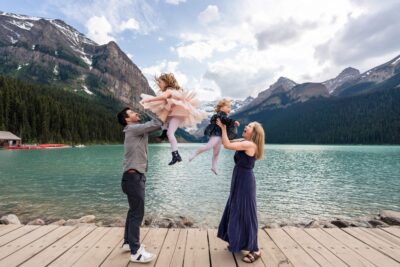 Family holiday photoshoot at Lake Louise. Mum and Dad throwing daughters in the air by the lakeshore. Lauren Hollamby Photography.