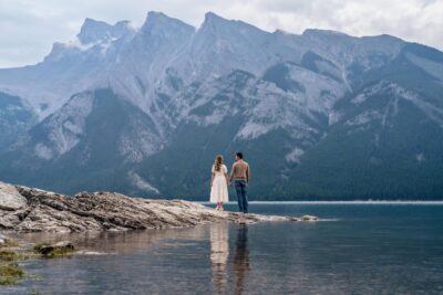 A photograph of a couple looking out over Lake Minnewanka. Holiday photoshoot by Lauren Hollamby Photography.